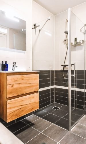 Salle de bain fonctionnelle à Amiens avec douche vitrée, meuble en bois, WC suspendu et carrelage noir et blanc.