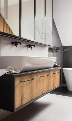 Double robinetterie noire à Amiens sur un meuble en bois foncé avec baignoire îlot partielle visible.